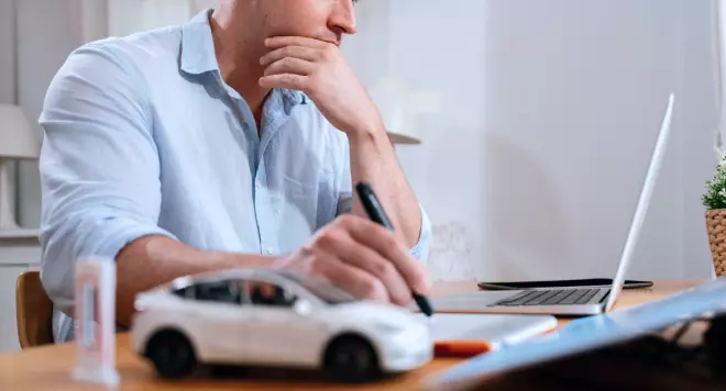 Mężczyzna siedzący przed laptopem z modelem auta na biurku