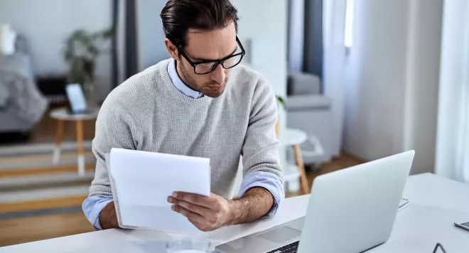 Mężczyzna z dokumentami siedzący przed laptopem